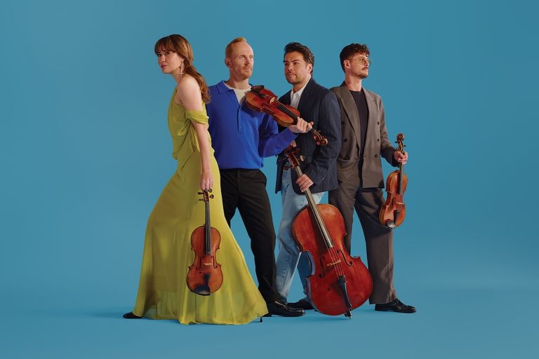 Australian String Quartet posing with violins and a cello against a vibrant blue studio backdrop.